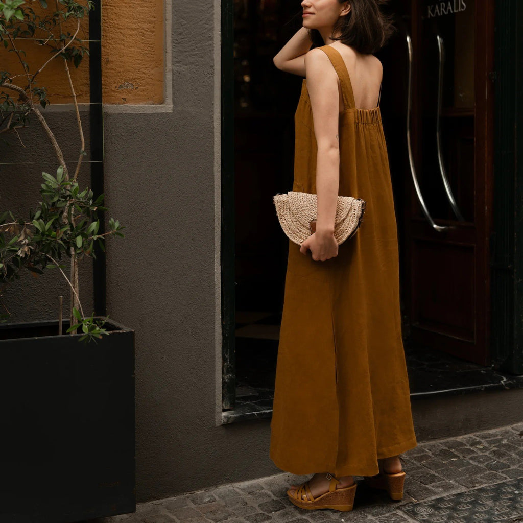 3. Back view of woman in bronze linen dress with elasticated back, holding a woven clutch, standing in a doorway