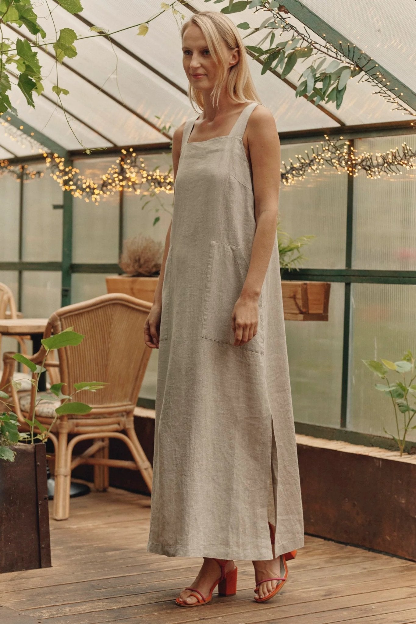 2. Woman in a long A-line linen dress with side slits and front pockets, standing in a greenhouse with decorative lights