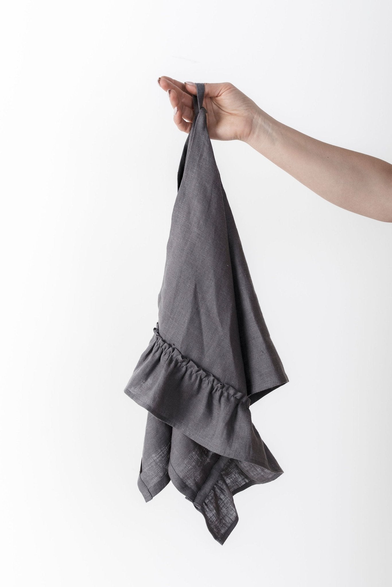 9. Hand holding a gray linen kitchen towel with ruffles against a white background