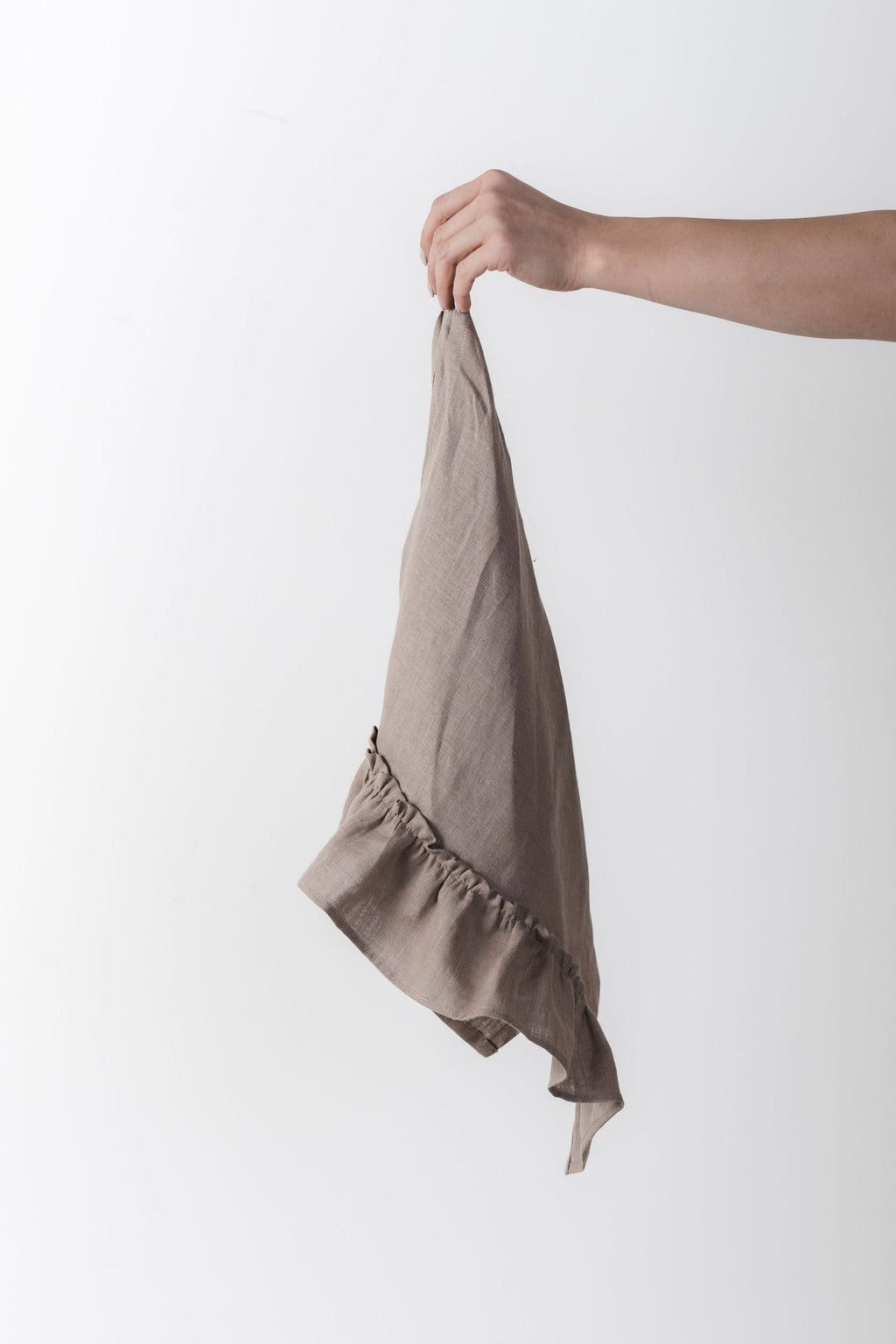 11. Hand holding a cappuccino-colored linen kitchen towel with ruffles against a white background