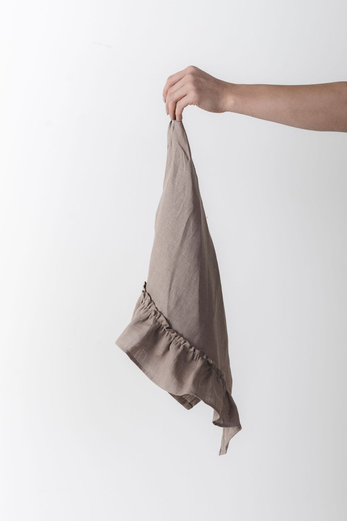 11. Hand holding a cappuccino-colored linen kitchen towel with ruffles against a white background