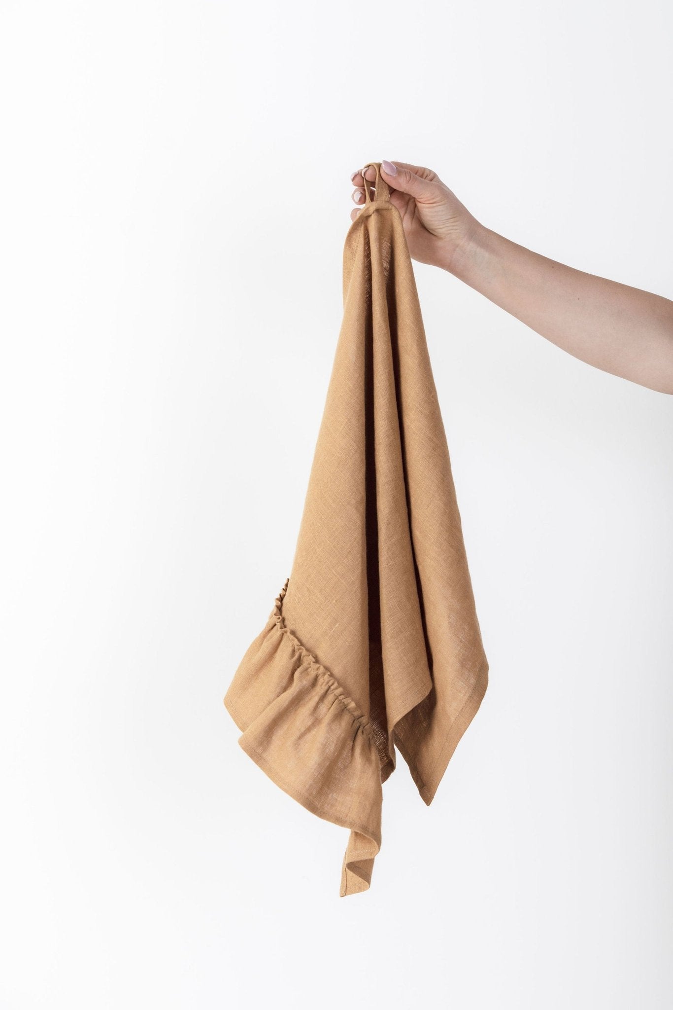 8. Hand holding a caramel-colored linen kitchen towel with ruffles against a white background