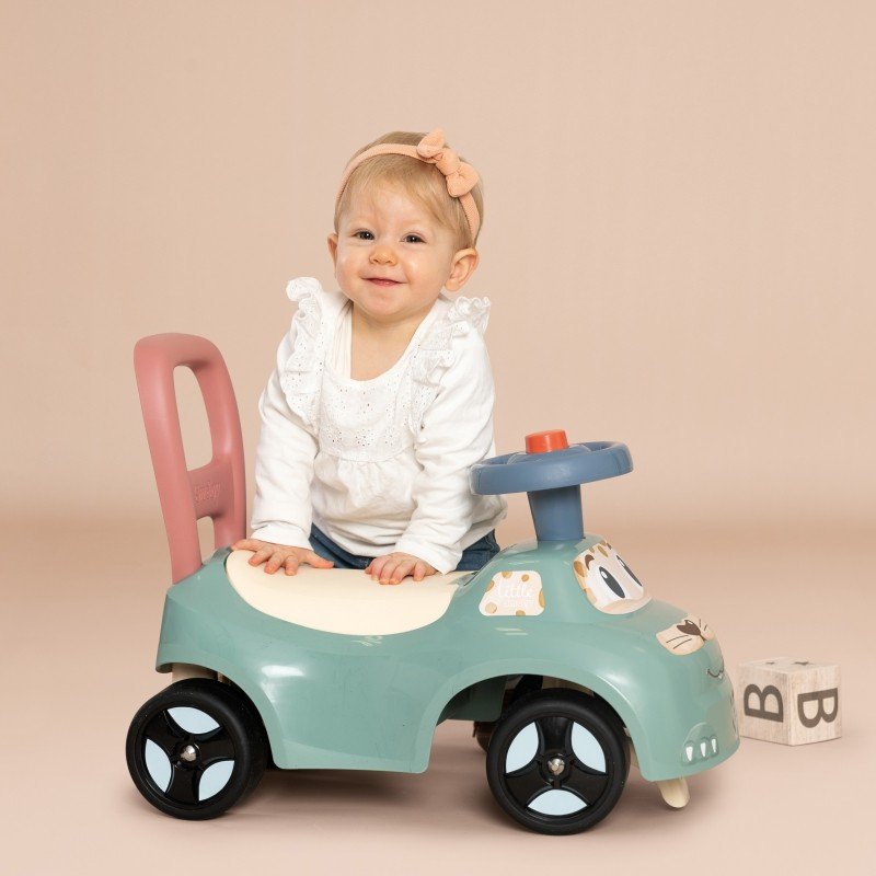 1. Smiling toddler sitting on Smoby Little Ride-on Pusher in pastel colors, indoor setting