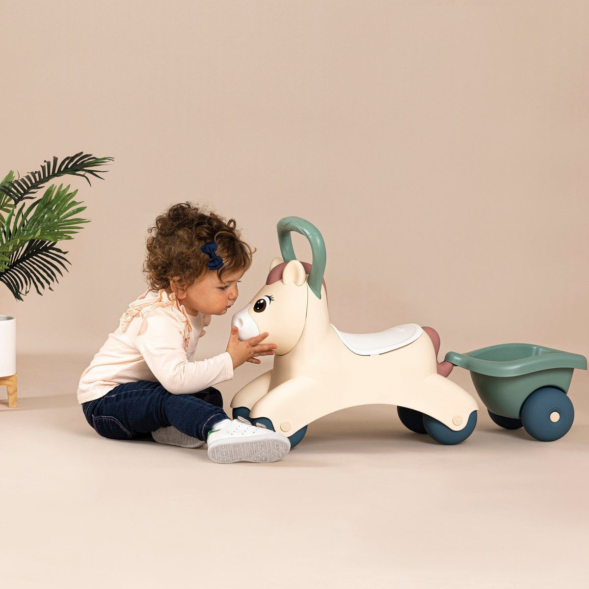 5. Child kissing beige pony ride-on with green trailer on a beige background
