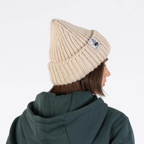 1. Woman wearing beige ribbed beanie with Moomin logo, shown from side, against white background