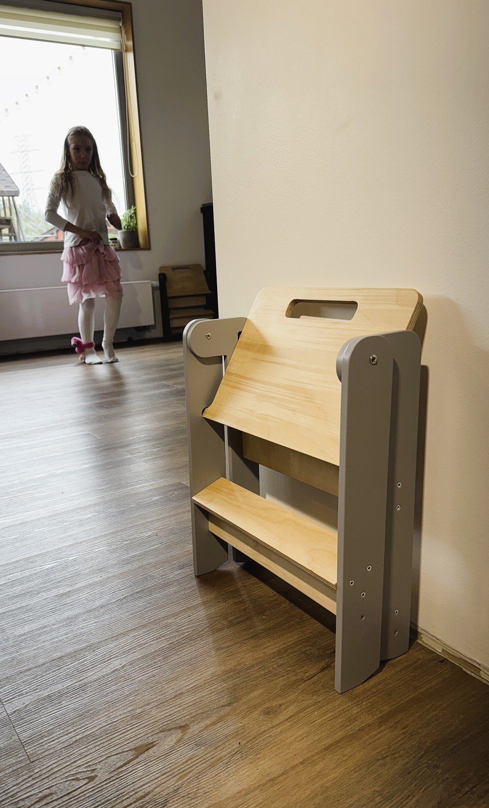1. Girl walking towards wooden step stool in a bright room with wooden floor