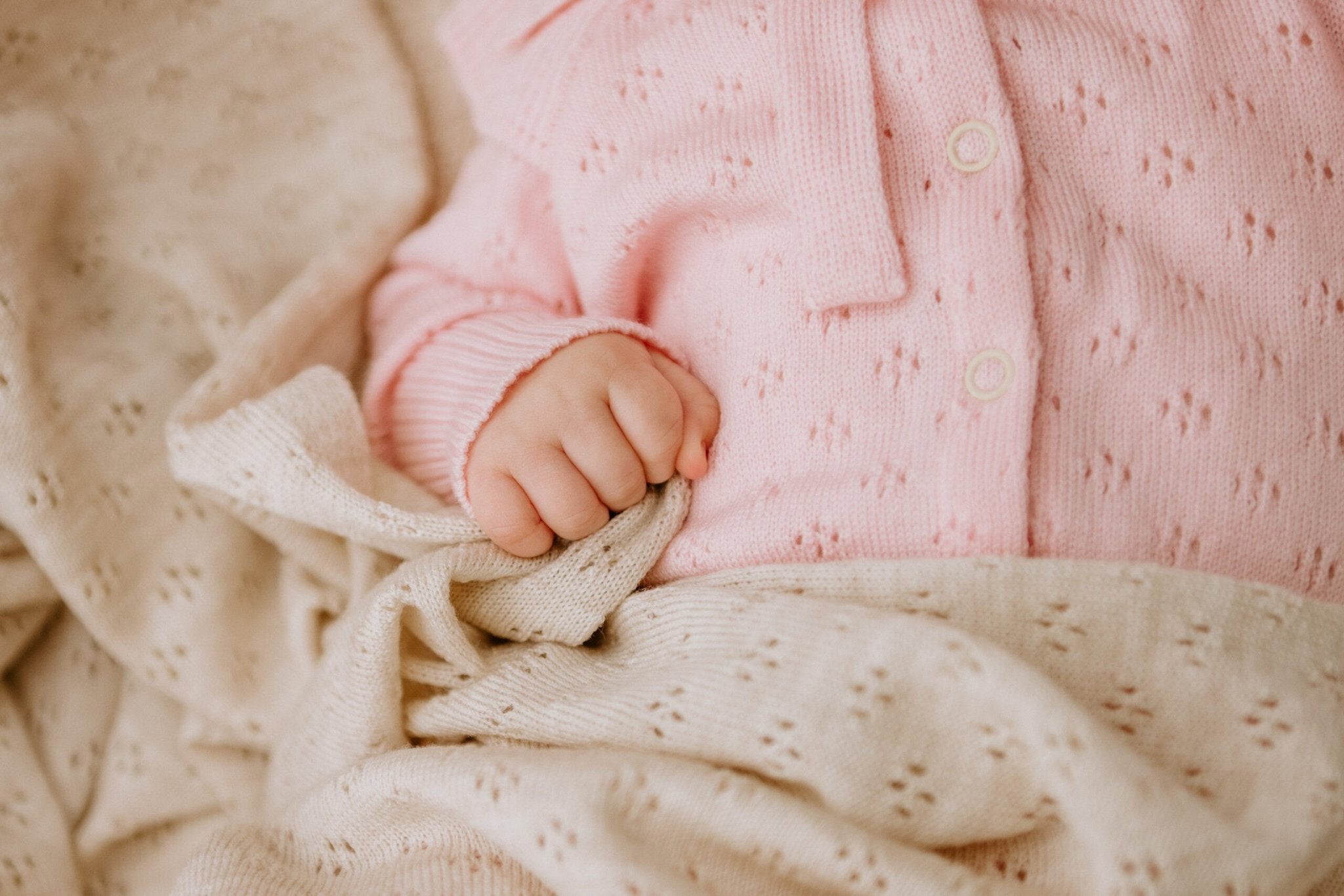 8. Close-up of baby's hand holding a beige merino wool blanket with floral pattern