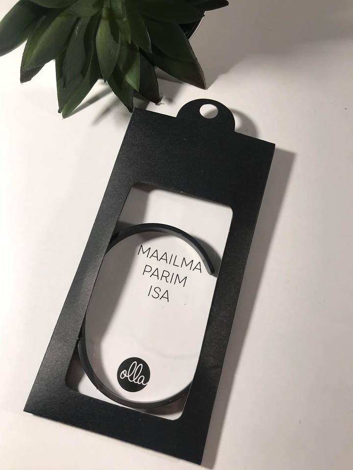 1. Black Olla bracelet in packaging with 'MAAILMA PARIM ISA' text, displayed on white surface with green plant