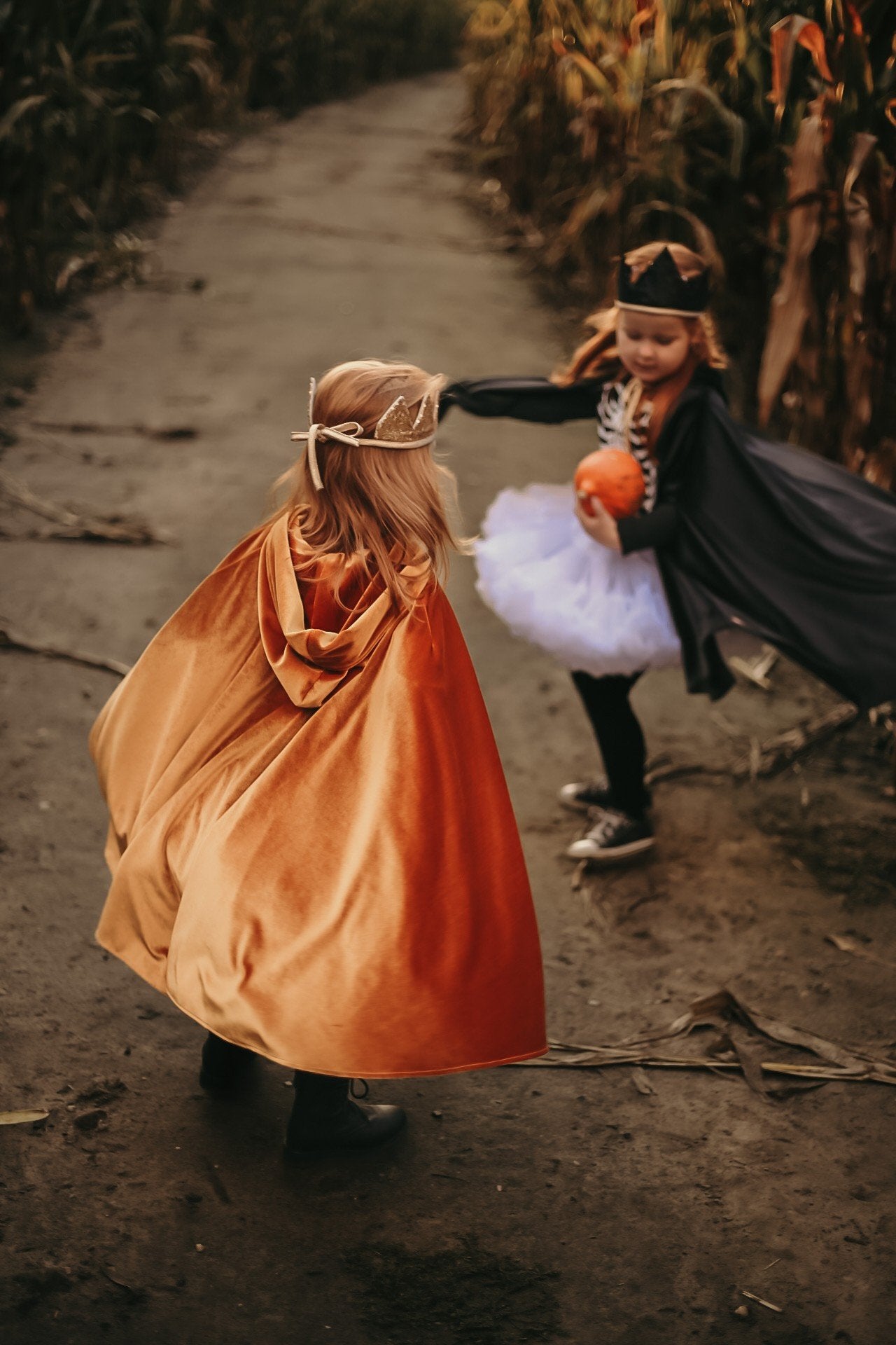 3. Two children playing in golden and black capes on dirt path