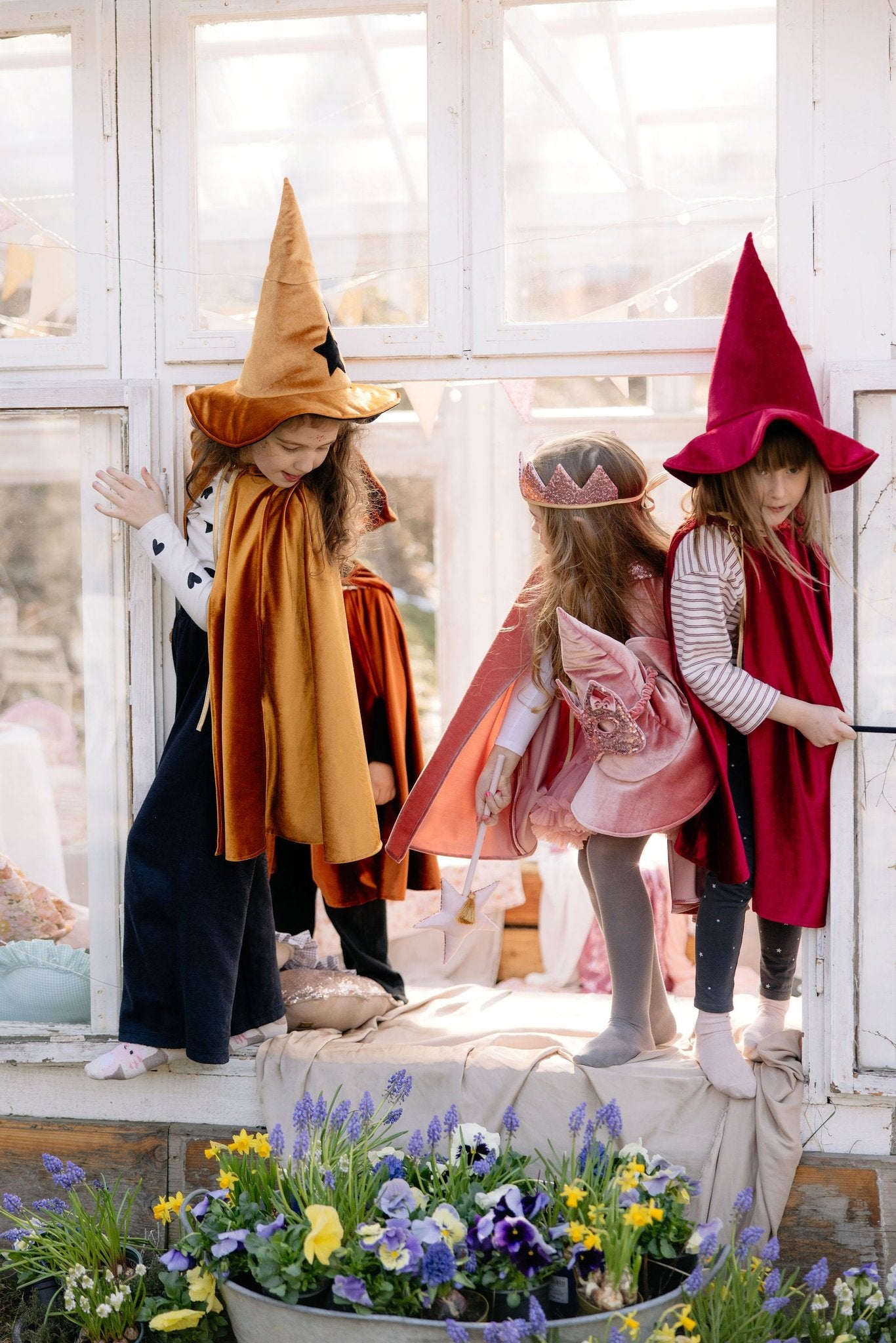 10. Children in golden, pink, and red capes by window with flowers
