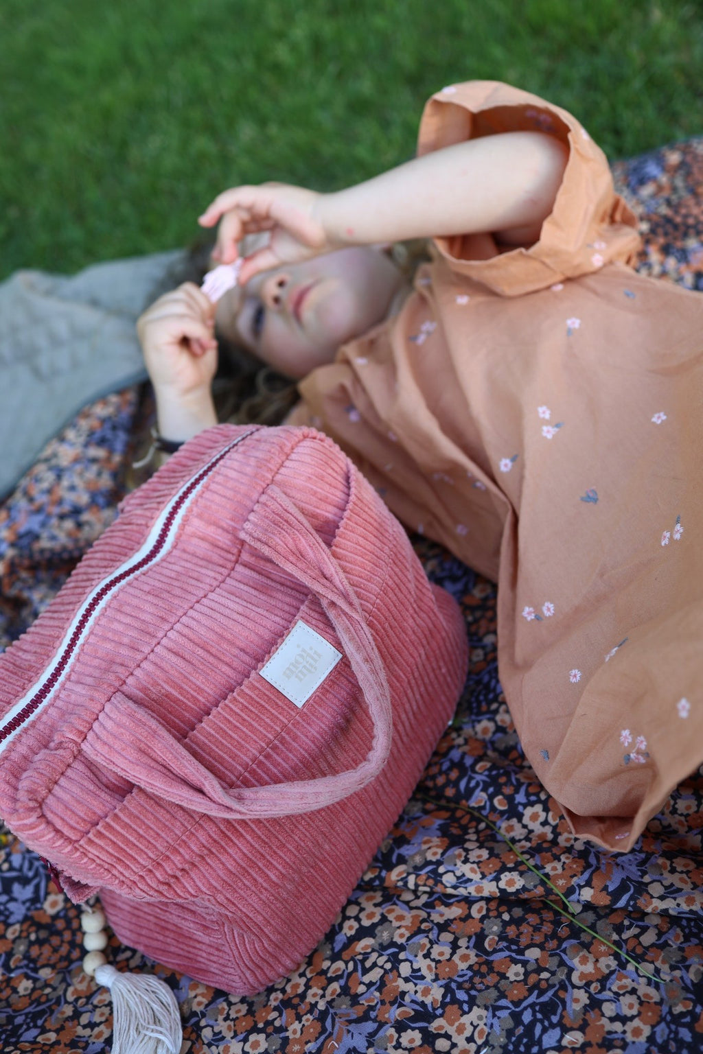 1. Child lying on floral blanket with large coral makeup bag nearby, showcasing outdoor use