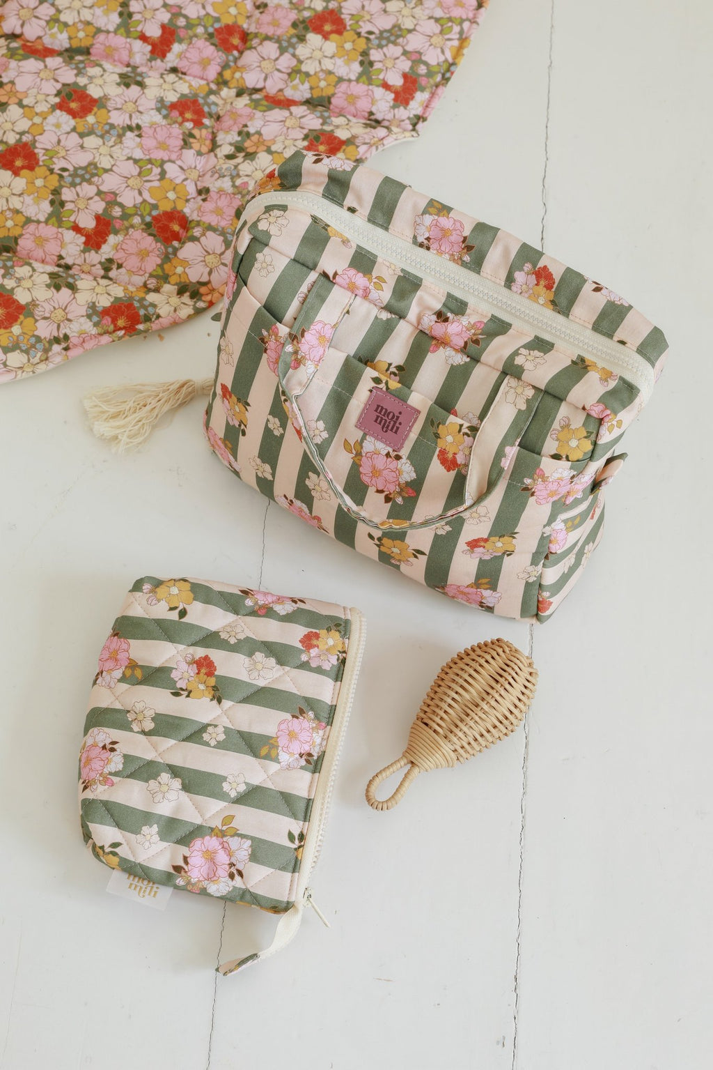2. Flat lay of two green striped floral makeup bags on white floor with decorative mat, showcasing Moi Mili logo