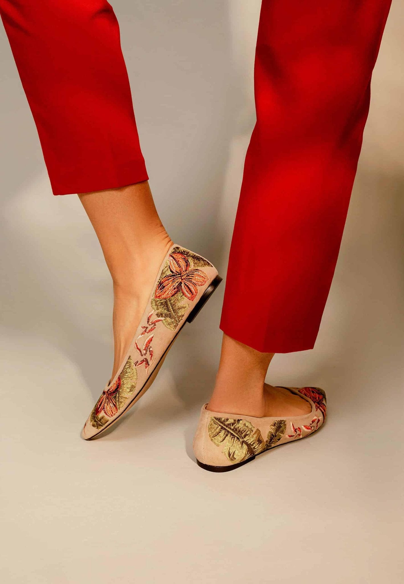 3. Woman showing back view of Mangará Pindaiva Ballerinas in red suede with floral embroidery, styled with red pants