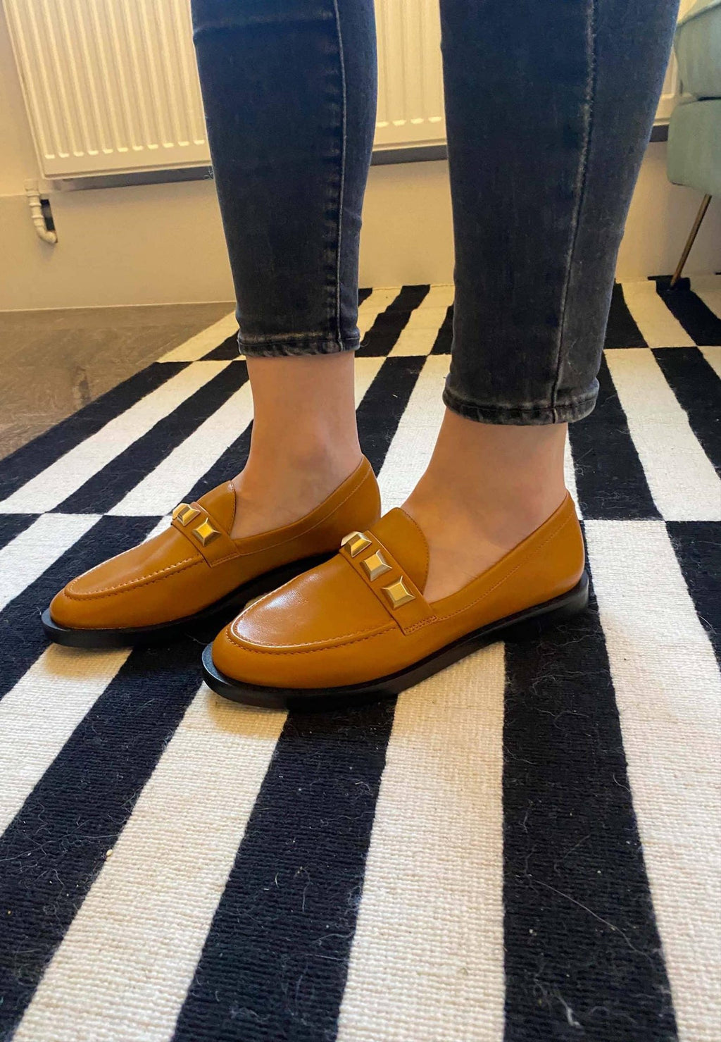 14. Women's brown Mangará Caete leather loafers with metal studs, worn with jeans on a striped rug