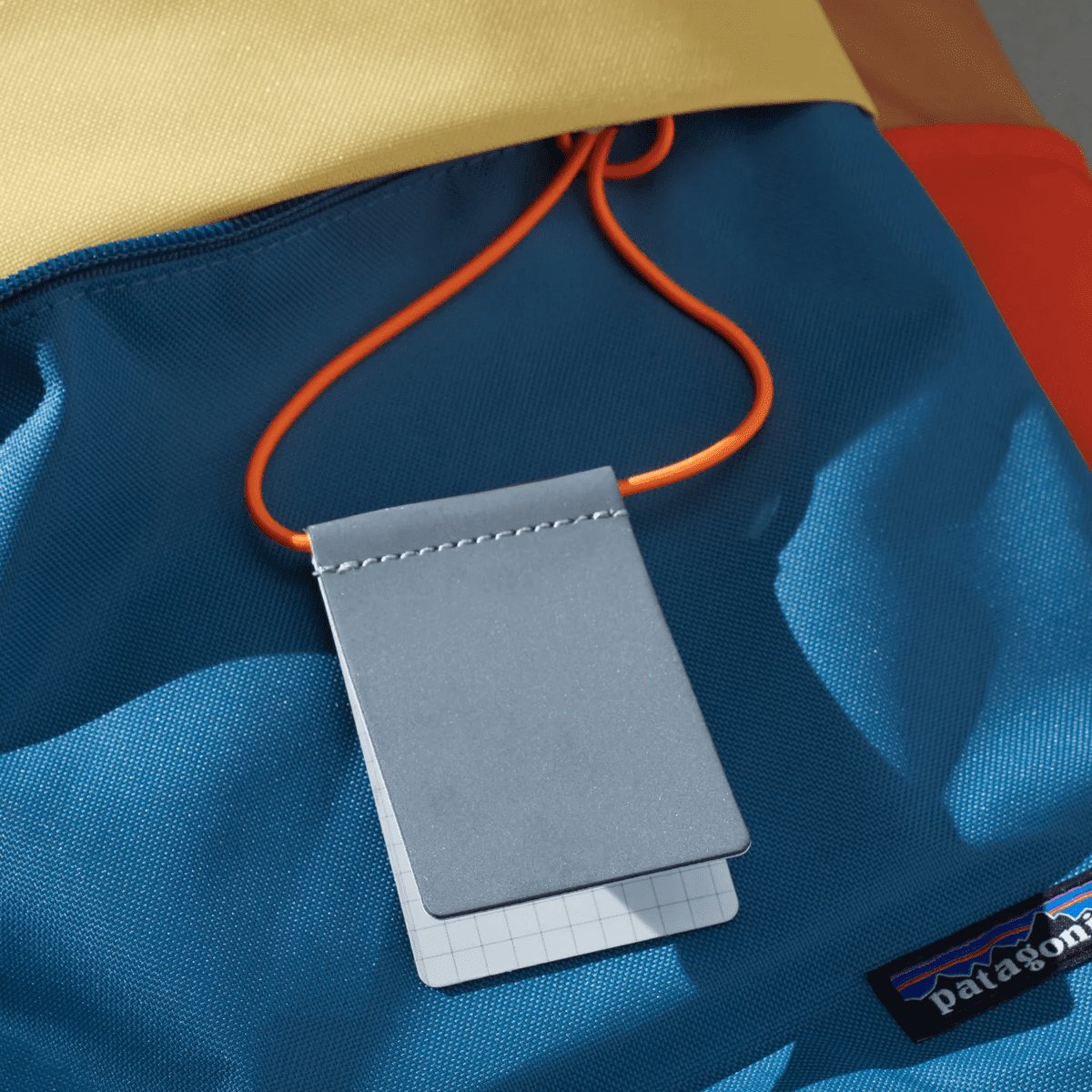 6. Grey MARCH Reflective Luggage Tag with neon orange strap on blue bag, emphasizing visibility