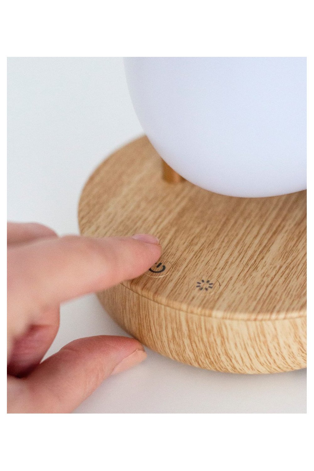 3. Close-up of hand adjusting controls on wooden base of pink bird lamp