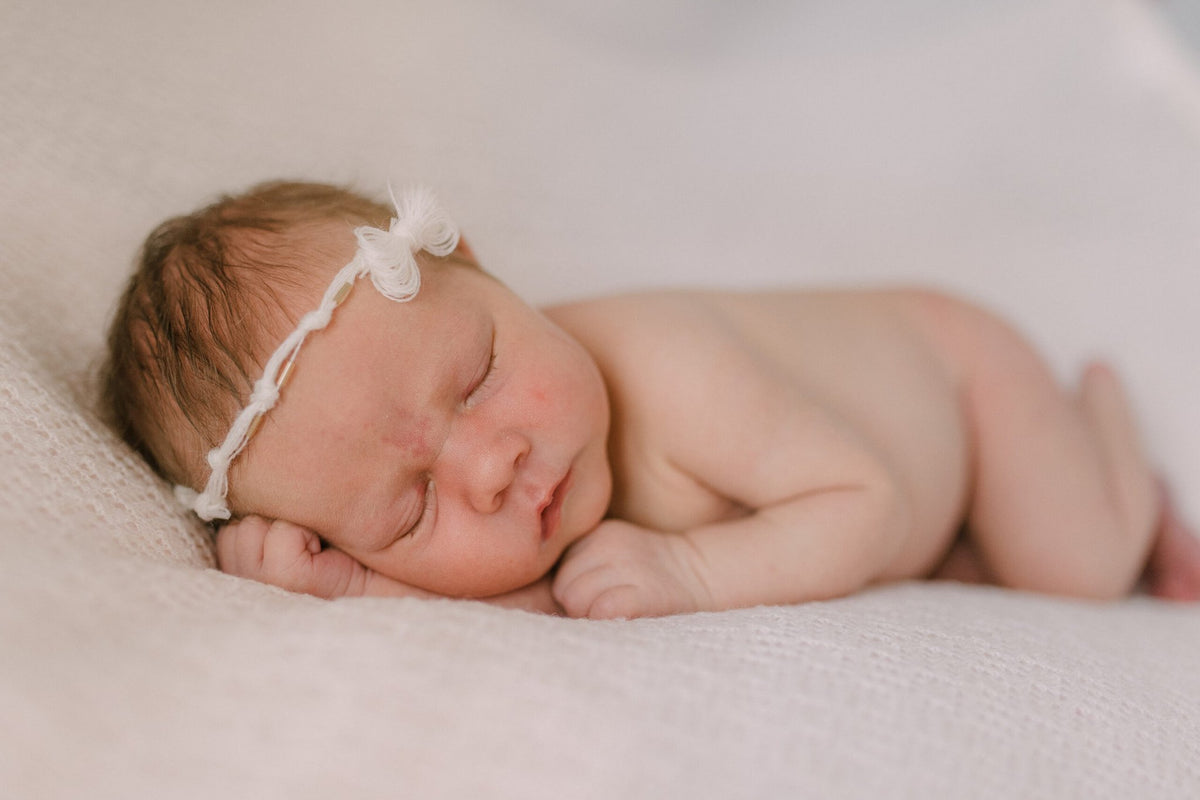 1. Newborn baby sleeping on white merino wool blanket wearing headband