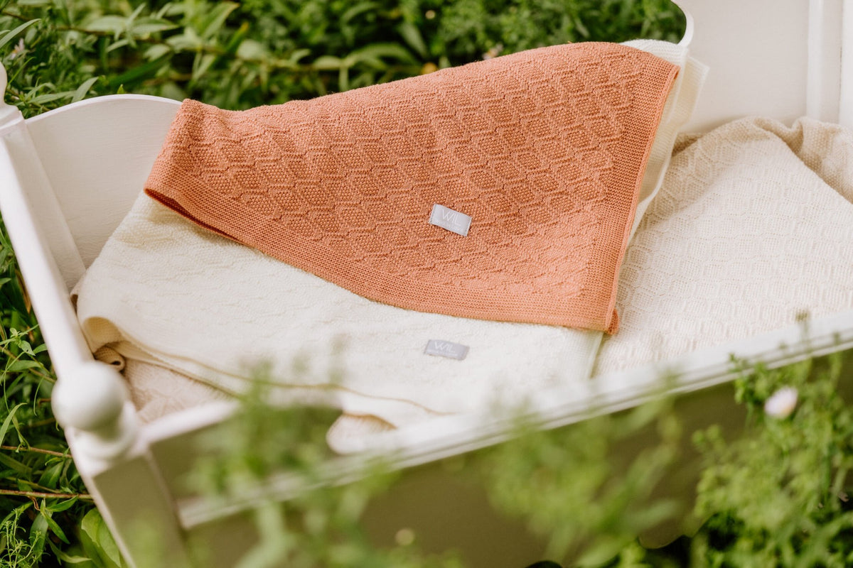 4. Orange merino wool blanket folded on cream blanket in outdoor setting