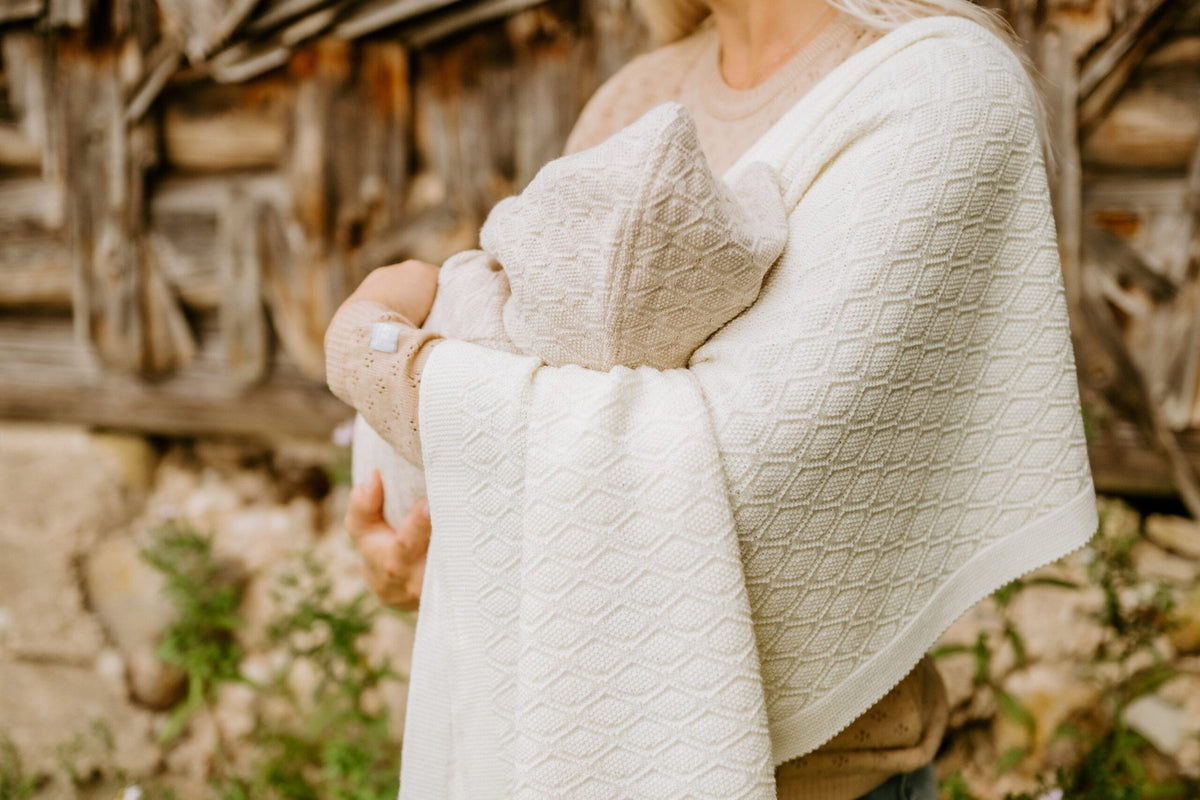 10. Woman holding baby wrapped in cream merino wool blanket in rustic outdoor setting