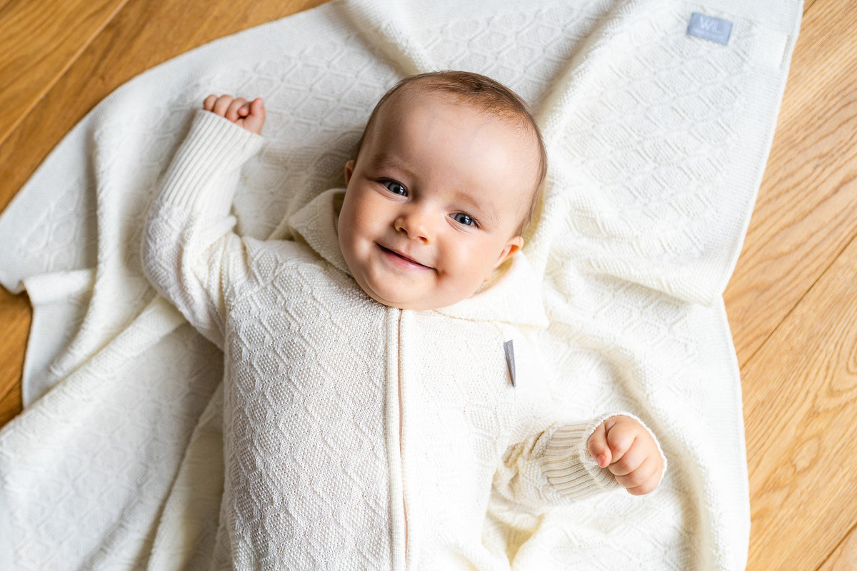 3. Smiling baby lying on cream merino wool blanket in indoor setting