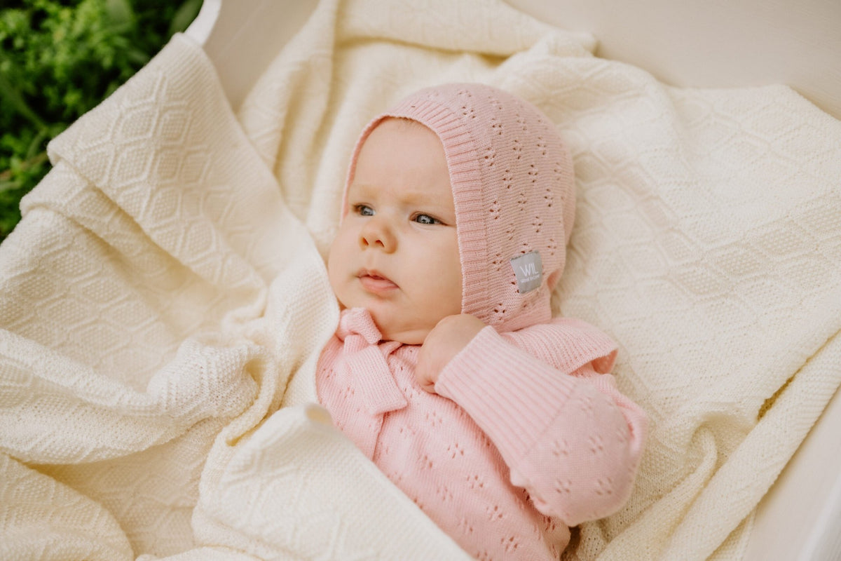 12. Baby in pink bonnet wrapped in cream merino wool blanket in outdoor setting
