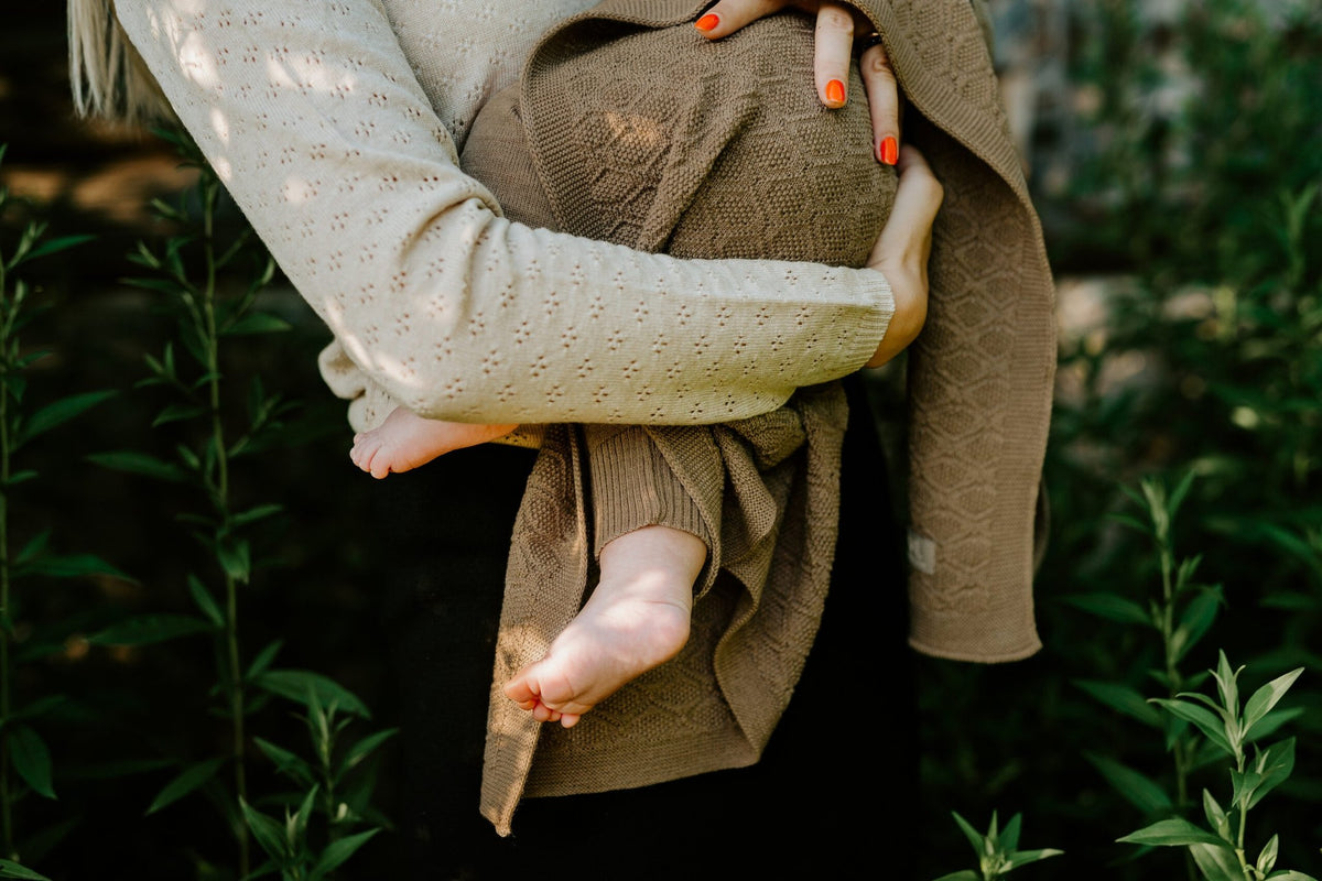 7. Baby wrapped in brown merino wool blanket held by adult in outdoor setting