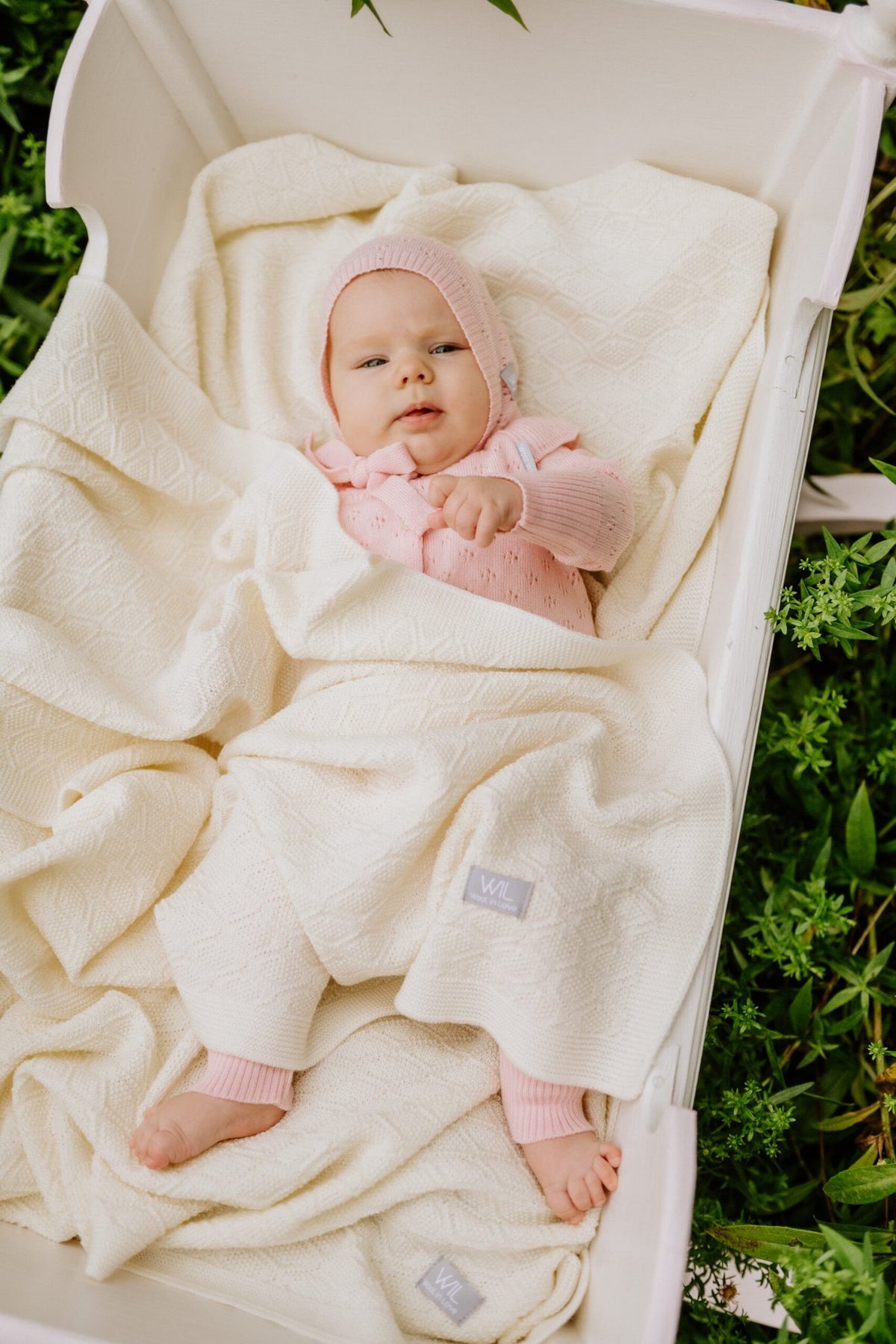 11. Baby in pink outfit lying on cream merino wool blanket in outdoor setting