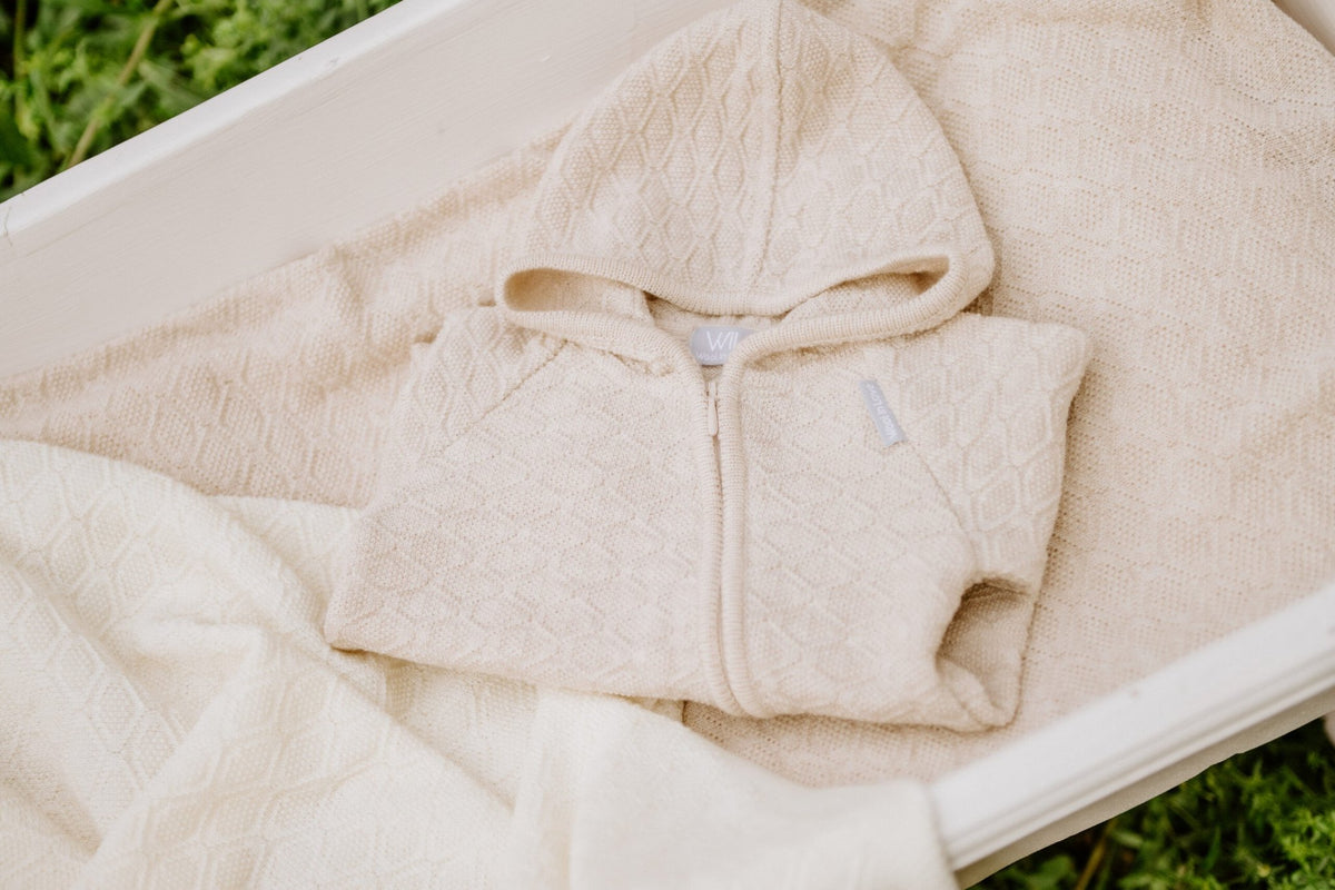 6. Cream merino wool baby hoodie on blanket in outdoor setting