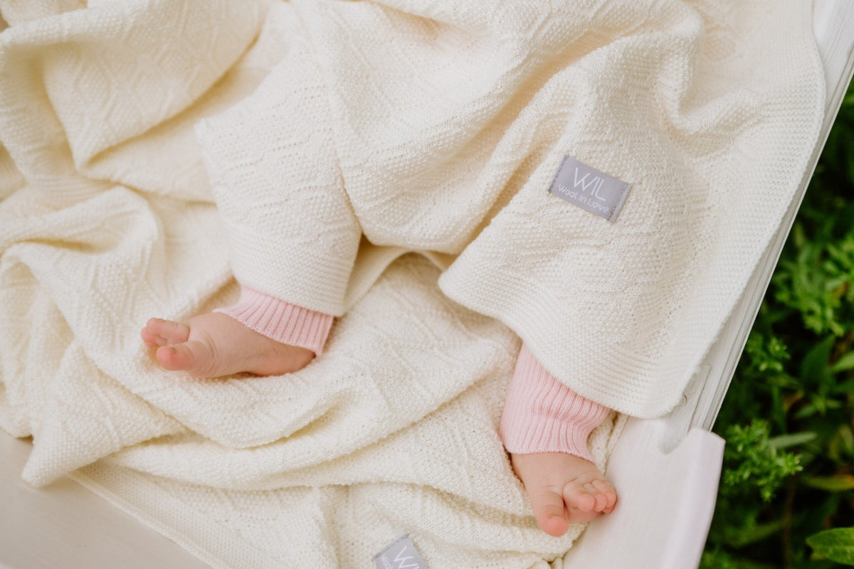 2. Close-up of baby feet wrapped in cream merino wool blanket with visible brand tag