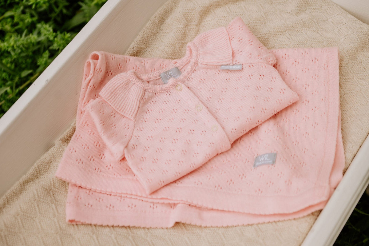 15. Pink merino wool baby blanket and outfit in white cradle with greenery