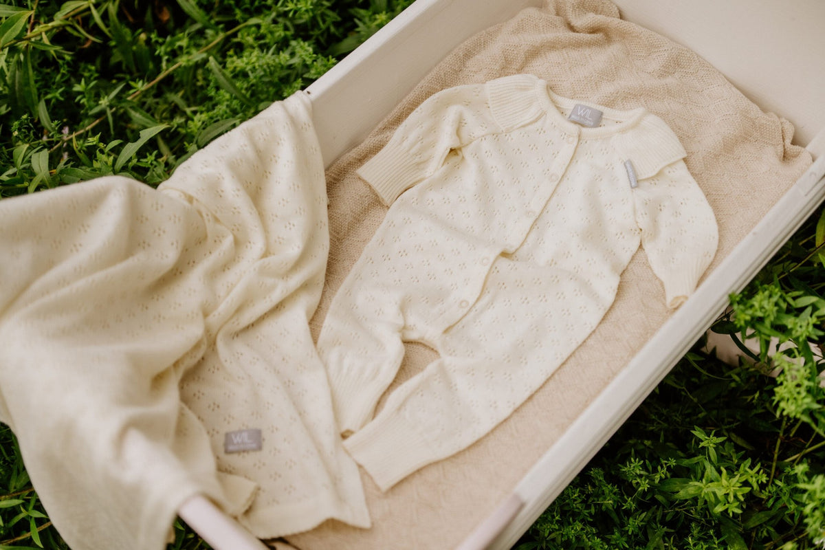 12. Cream merino wool baby blanket and outfit in white cradle with greenery