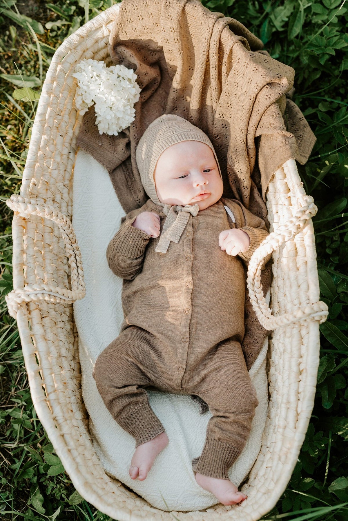11. Baby in brown outfit with beige merino wool blanket in woven basket outdoors