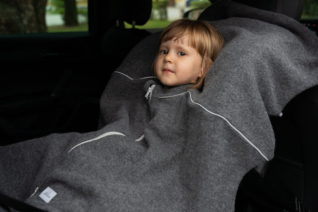 2. Child sitting in car seat wearing grey merino wool poncho with visible reflective details
