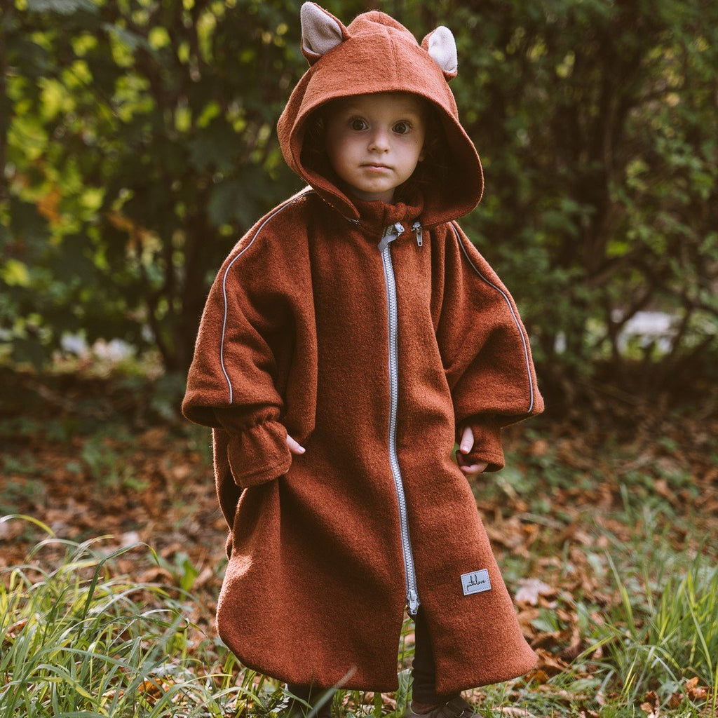 1. Child wearing brown merino wool poncho with fox ears hood standing in a forest setting