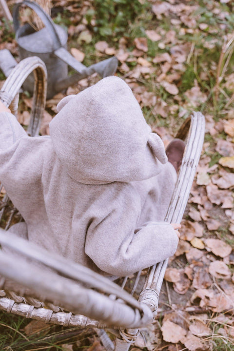4. Child sitting in wicker chair wearing beige hooded merino wool poncho