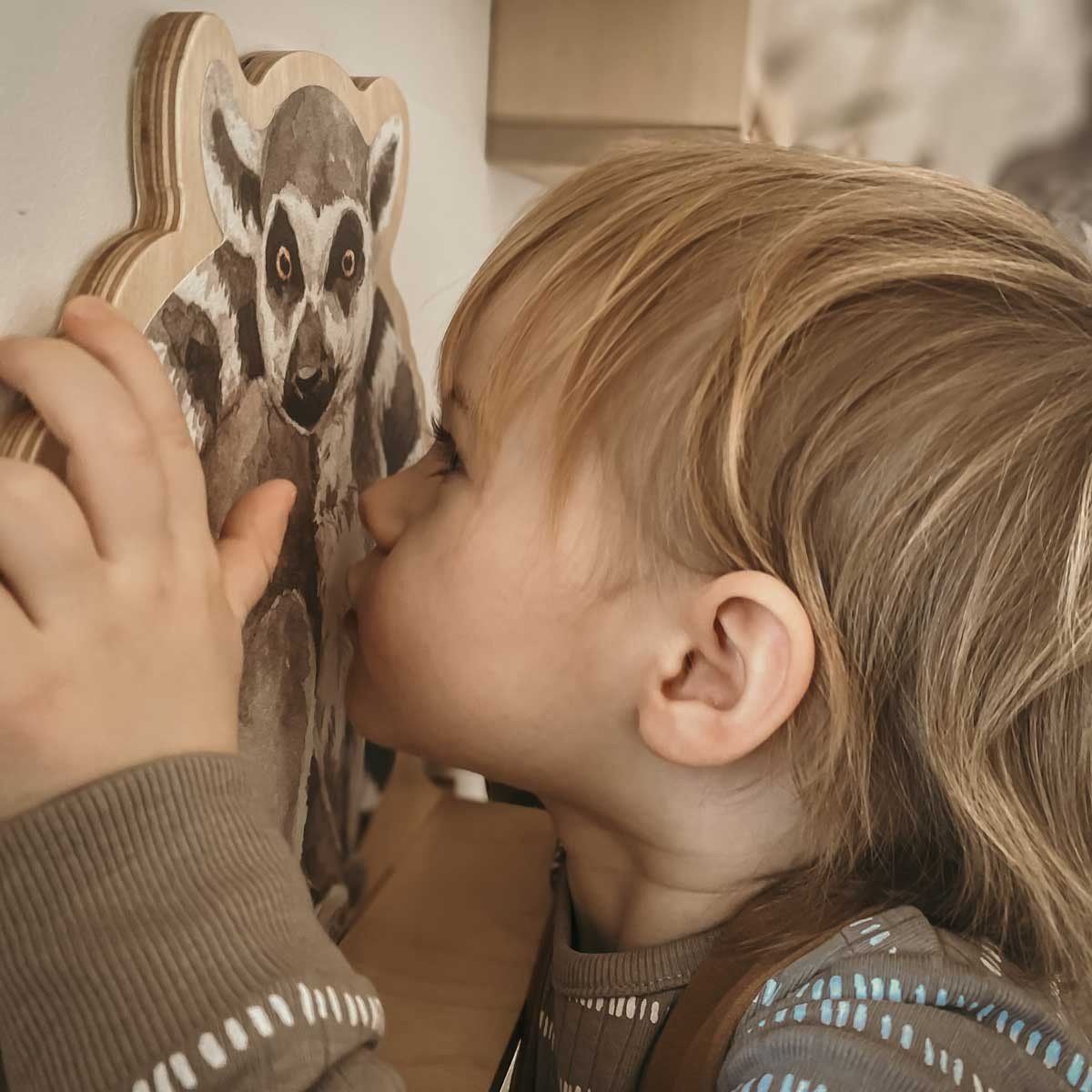 1. Child closely examining Dekornik mini wall shelf with lemur design in a playful setting