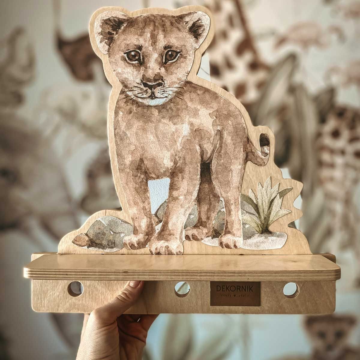 3. Close-up of Dekornik mini wall shelf with lion design held by a hand, showing plywood texture and brand logo