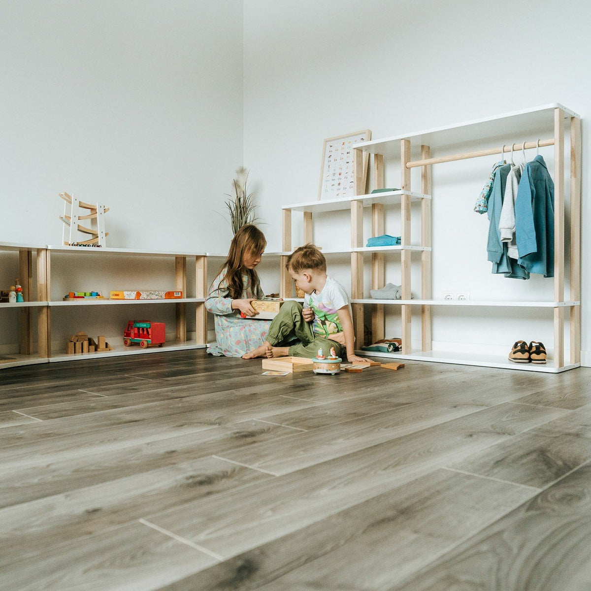 1. Two children playing near a modular Montessori bookshelf filled with toys and clothes in a playroom