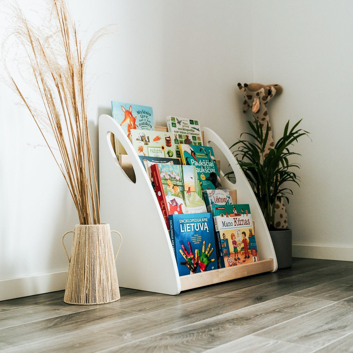 7. Montessori bookshelf with books in a corner of a room with plant and giraffe decor