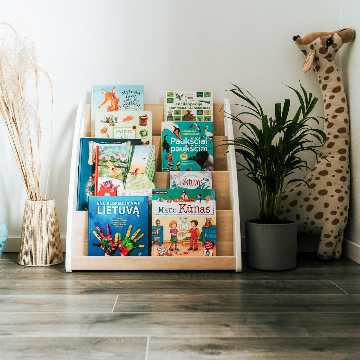 4. Montessori bookshelf filled with children's books next to a plant and giraffe decor in a child's room