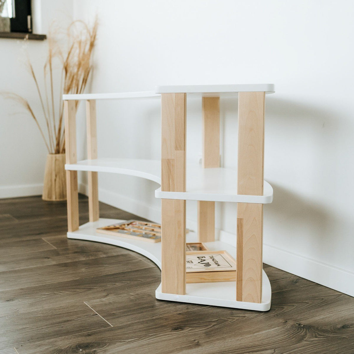 3. Side angle of modular Montessori shelf with three white shelves and natural wood supports, showing empty shelves and wooden flooring.