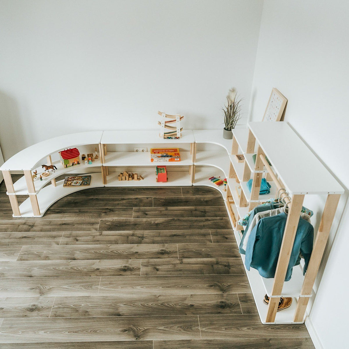 5. Top view of a playroom with modular Montessori shelves in white and natural wood, displaying toys and clothes