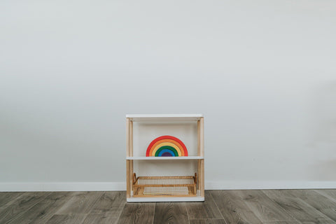 1. Modular Montessori shelf with three shelves, featuring a rainbow toy, against a white wall and wooden floor