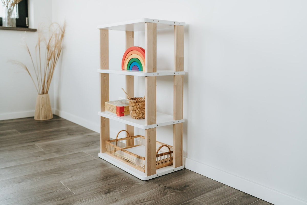 1. Modular Montessori Shelf Straight Mini with four shelves in a children's room, featuring natural wood and white painted finish, holding toys and baskets, against a white wall and wooden floor.