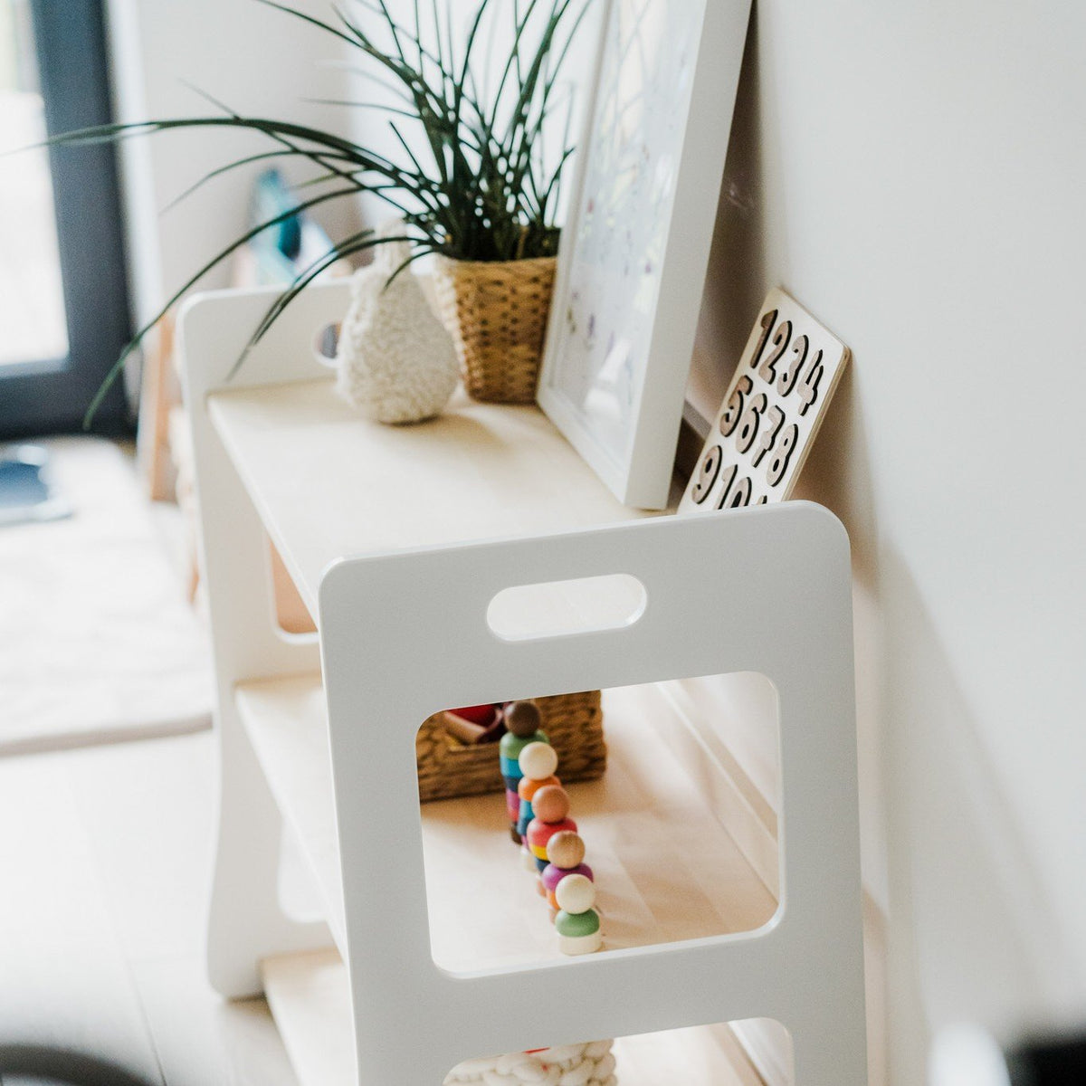 6. Side view of Montessori toy shelf with toys and decor, featuring a white and natural wood finish