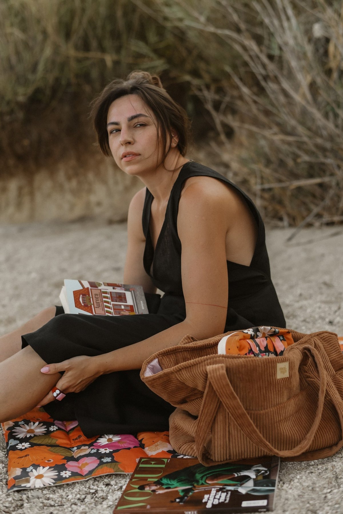 8. Woman sitting on beach with caramel velvet weekender bag and book