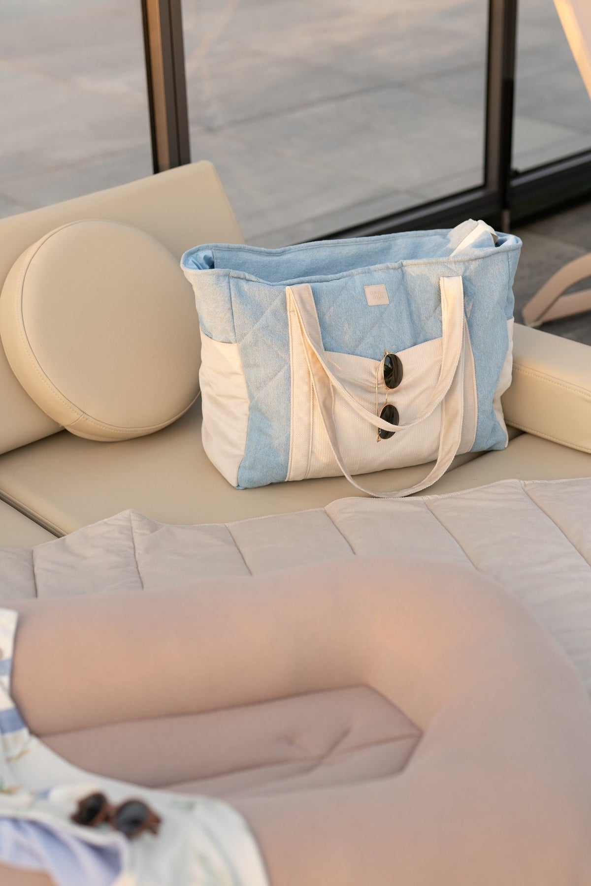 3. Blue and beige weekender bag with buttons on a beige lounge chair in a sunlit outdoor setting