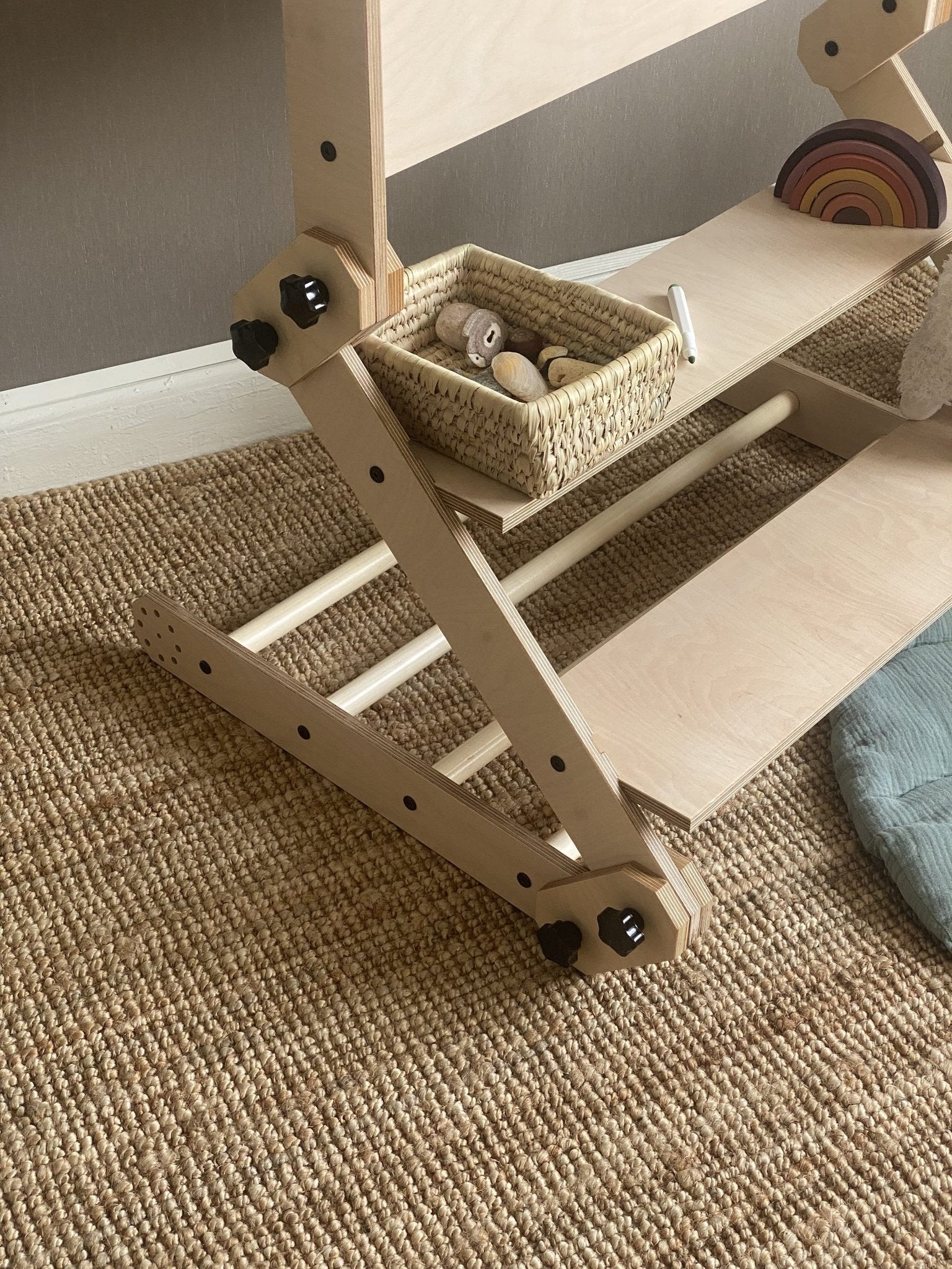 5. Close-up of Montessori climbing set base with wooden rungs and a basket of toys on a woven rug.