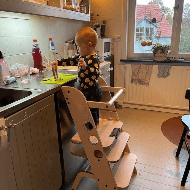 1. Toddler using wooden Montessori learning tower at kitchen counter