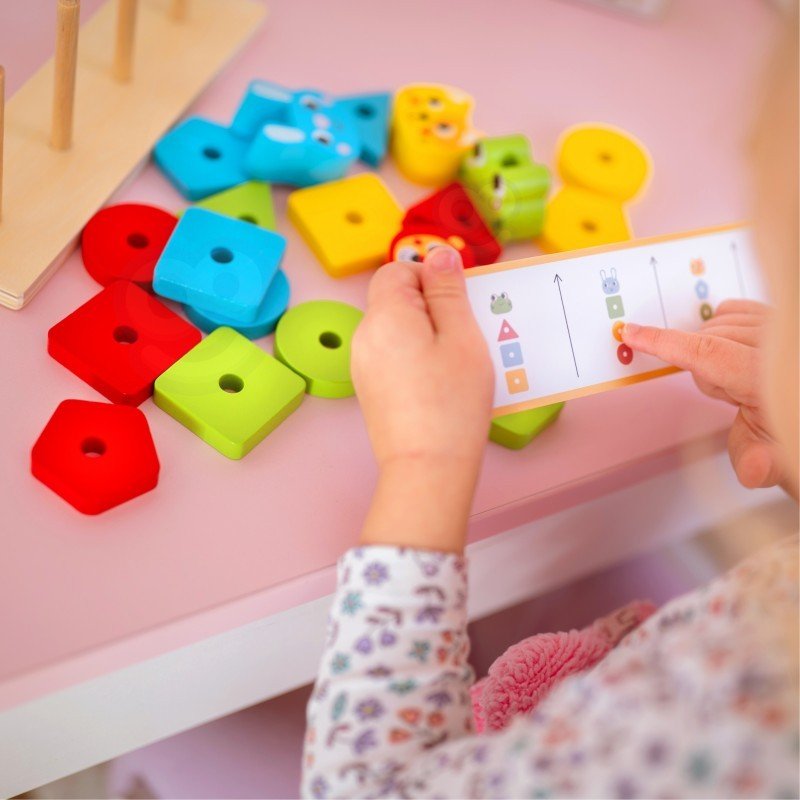 8. Child holding pattern card with colorful blocks scattered on pink table
